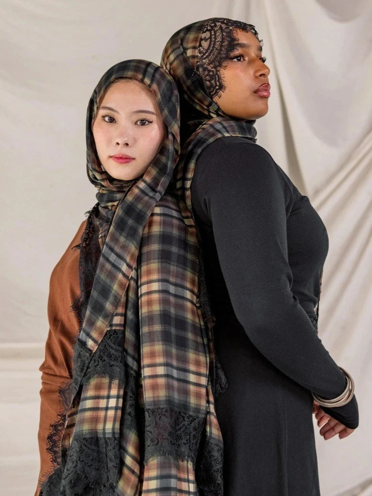 A woman wearing a plaid hijab scarf over a black top and brown garment.