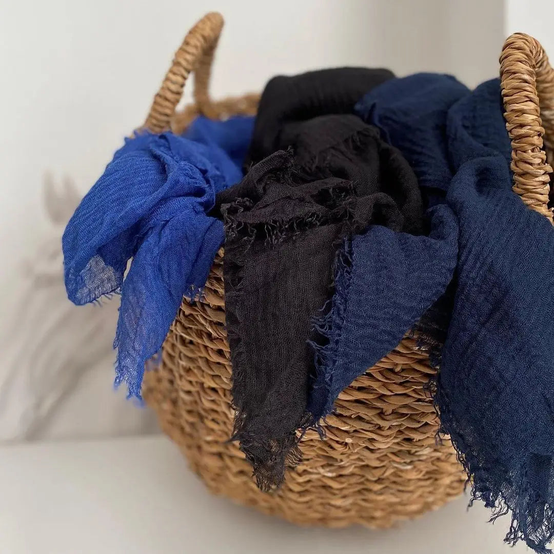 Geflochtener Korb gefüllt mit verschiedenen dunkelblauen und schwarzen crinkle Baumwoll-Hijab-Schals.
