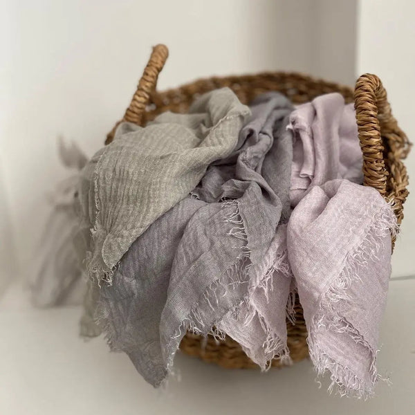A bundle of elegant crinkle cotton hijab scarves in shades of gray and lilac resting in a woven basket.