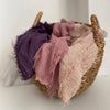 Gewebter Korb gefüllt mit Hijab-Schals aus Crinkle-Baumwolle in Violett, Rosa und Beige.