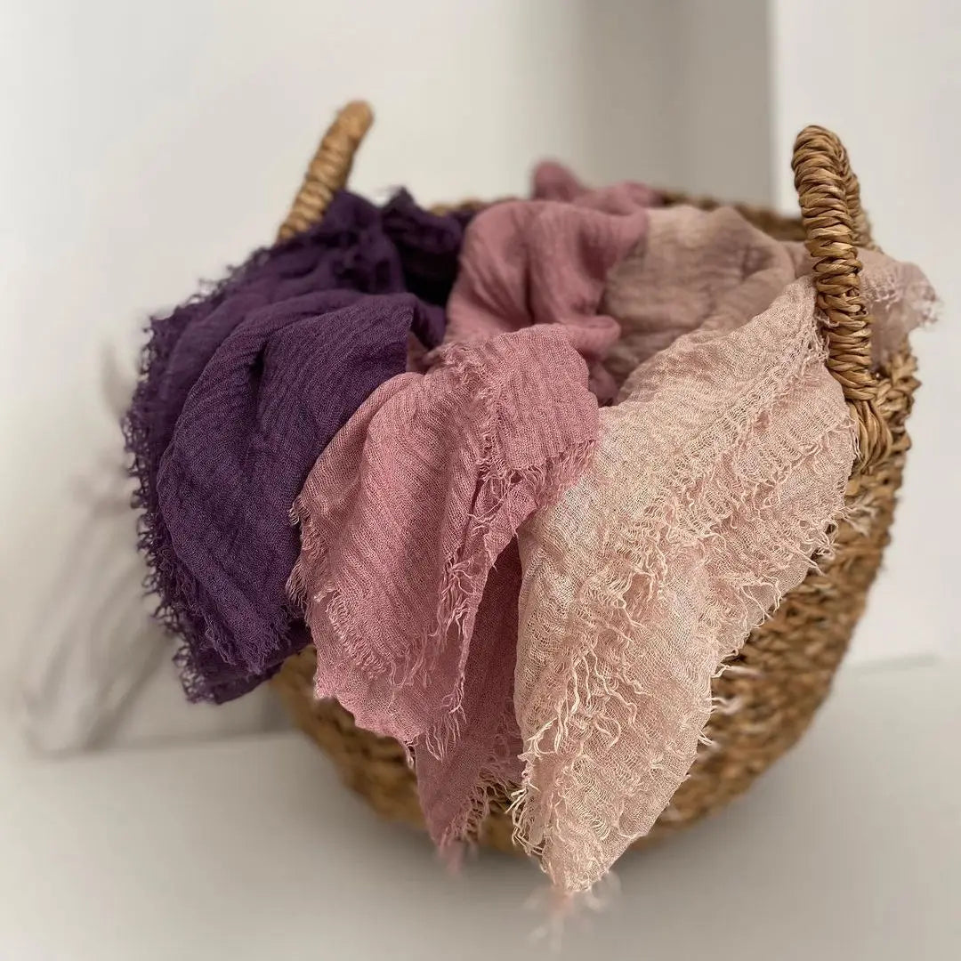 Gewebter Korb gefüllt mit Hijab-Schals aus Crinkle-Baumwolle in Violett, Rosa und Beige.