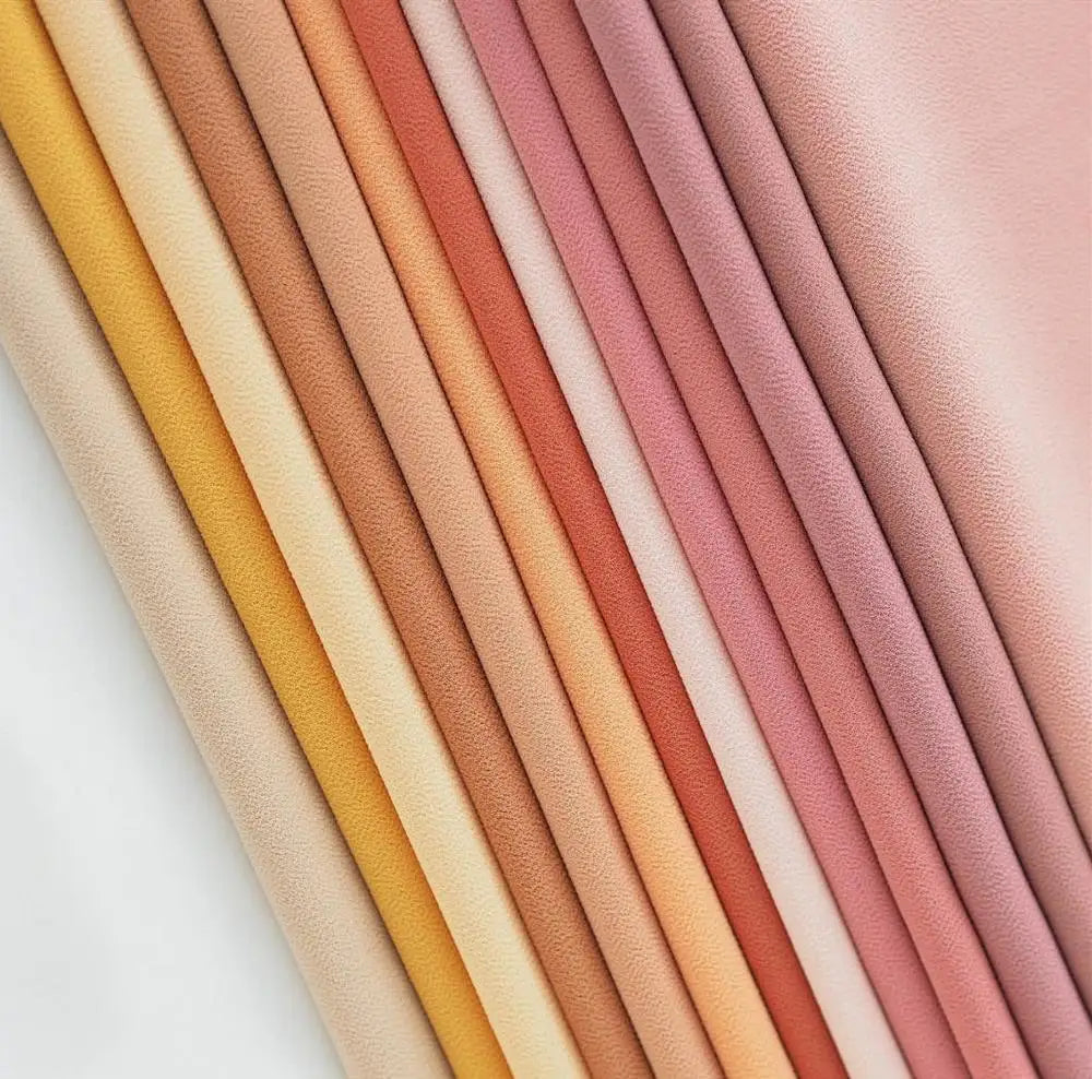 Exposición vertical de varios rollos de pañuelos de chifón premium en tonos pastel suaves.