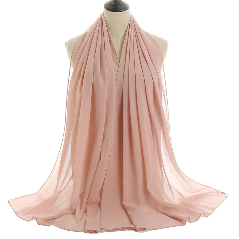 Un pañuelo de chifón color rosa empolvado y fluido drapeado alrededor del cuello de un maniquí.