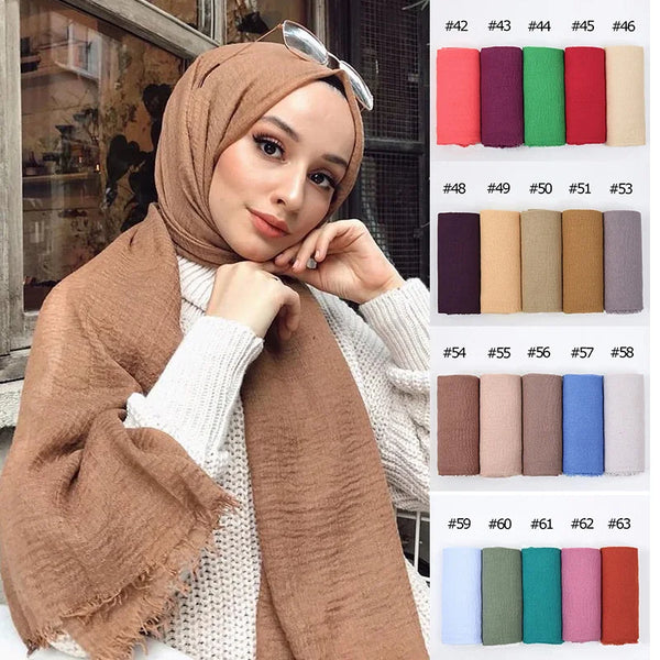 A woman models a brown crinkle cotton hijab scarf draped over her shoulder, with color swatches displayed nearby.